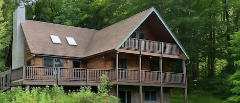 A two-story log cabin with a balcony, surrounded by lush greenery.
