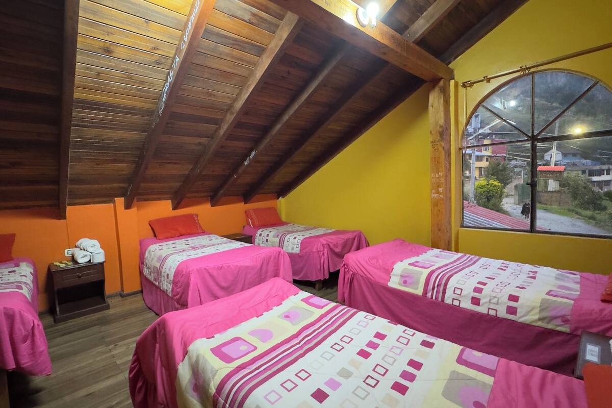 Un dormitorio con cuatro camas, vigas de madera en el techo y una ventana con vistas al exterior.