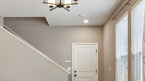 Ein modernes Wohnzimmer mit Esstisch für vier Personen, einem blauen Sofa, einer Treppe und einem großen Fenster mit Jalousien.
