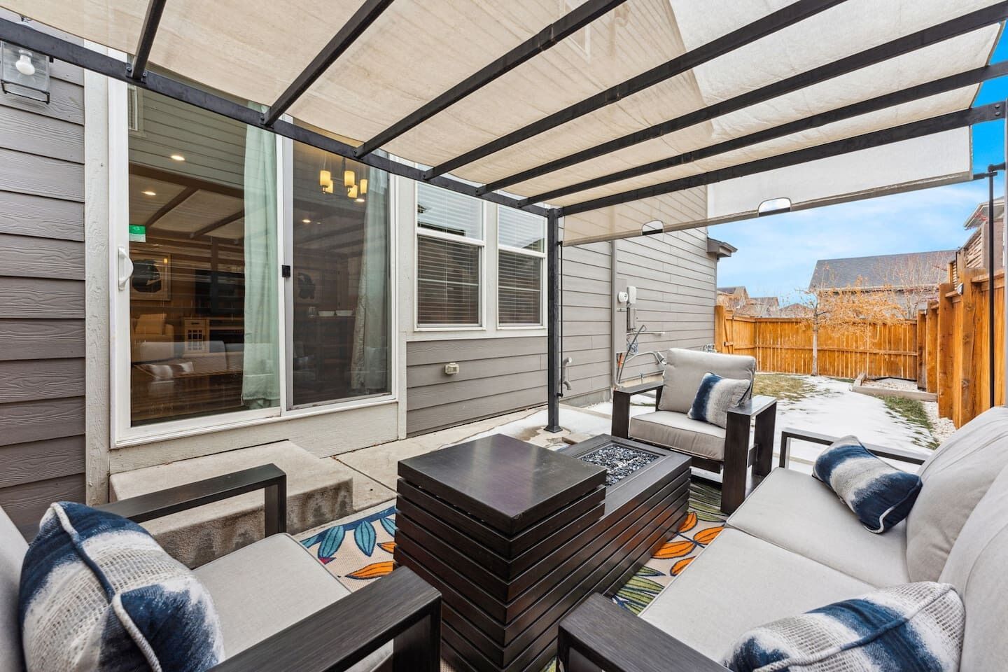 An outdoor patio with a covered seating area, a fire pit, and a view of a backyard.