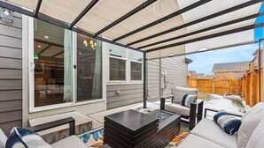 Eine Außenpatio mit überdachter Sitzgelegenheit, einem Feuerkorb und Blick auf einen Garten.