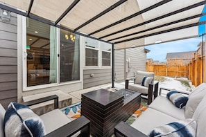 An outdoor patio with a covered seating area, a fire pit, and a view of a backyard.
