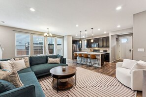 A modern living room with a sofa, a coffee table, and a kitchen area with bar stools.