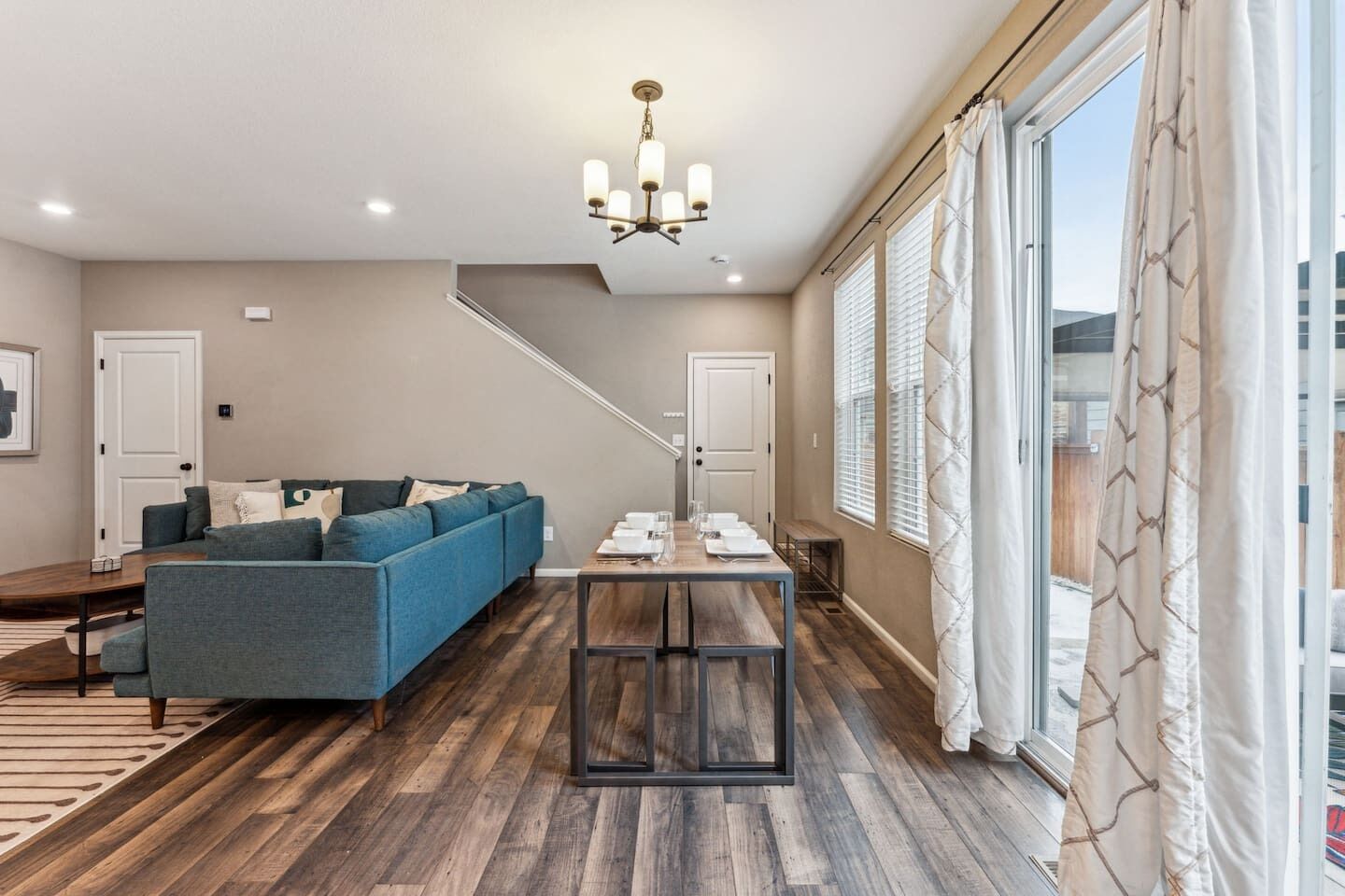 A modern living room with a sofa, a dining table set for six, and a staircase leading to another level.