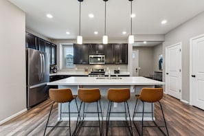 Una cocina moderna con una isla central, electrodomésticos de acero inoxidable e iluminación colgante.