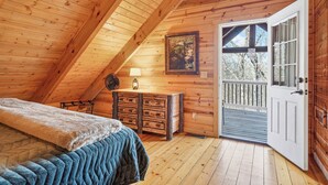 Une chambre confortable dans un chalet, avec un plafond en bois, un lit recouvert d’une courtepointe, une commode et une porte donnant sur un balcon.