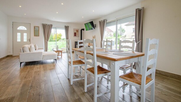 Ein geräumiges Wohnzimmer mit einem weißen Sofa, einem Holzespeisetisch mit weißen Stühlen und einem großen Fenster mit Vorhängen.
