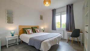 Ein Schlafzimmer mit einem Bett, Nachttischen, einem Sessel, einem Fenster mit Vorhängen und einer Wandleuchte.