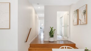 A modern interior with a wooden staircase, a white dining area, and a hallway leading to a glass door. - "Serenity & Poolside Sun" - (Scarborough)