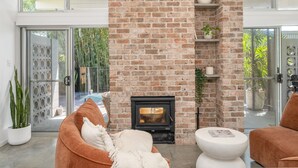 A modern living room with a brick fireplace, comfortable seating, and large glass doors leading to a balcony with a view of greenery. - "Serenity & Poolside Sun" - (Scarborough)