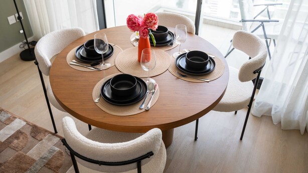 A round dining table with black plates, white chairs, and a vase with pink flowers. - Stayshort - Business Bay for 2 With Water Views (Dubai)