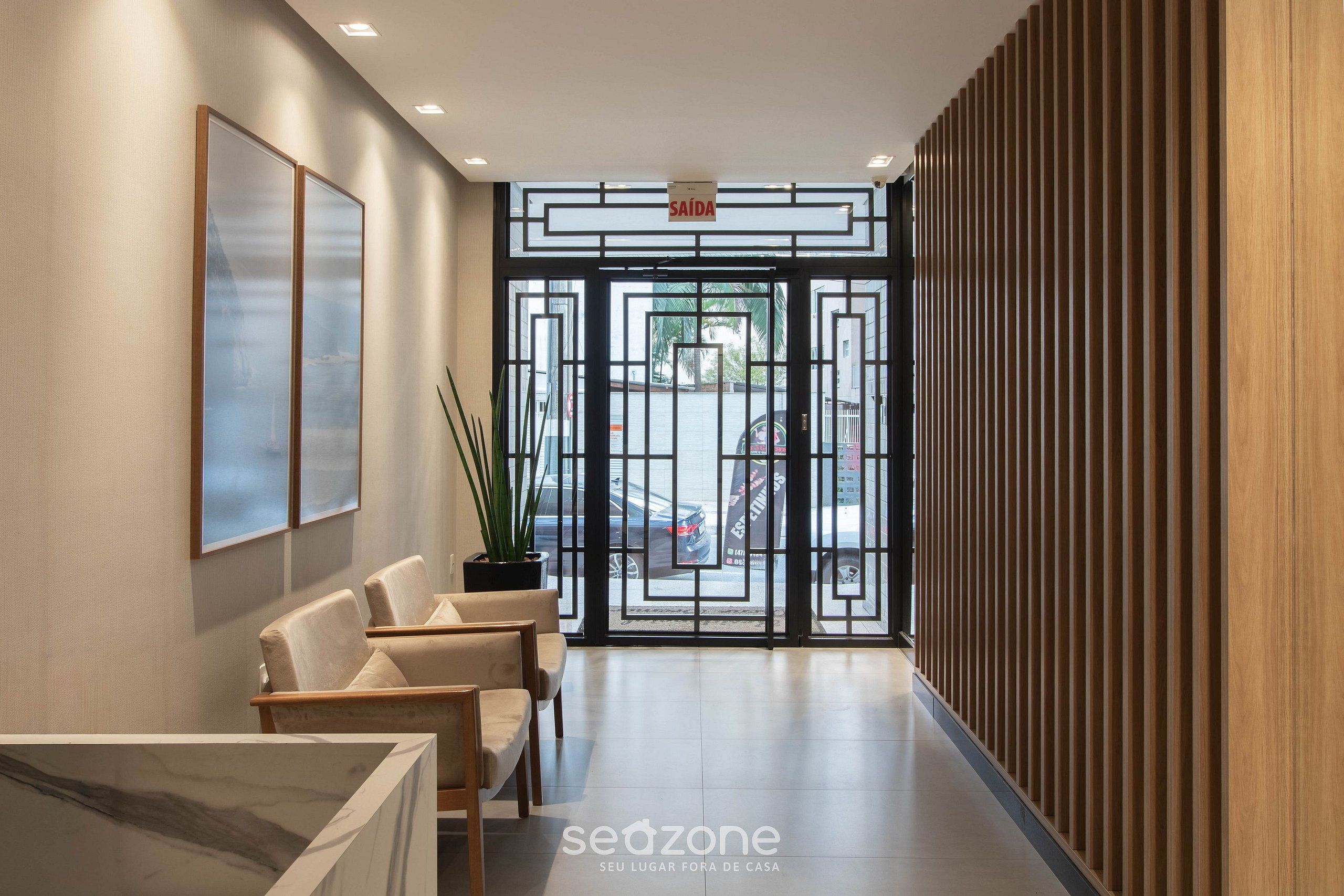 A reception area with a modern design, featuring a reception desk, seating area, and a view of the parking lot through a glass door.