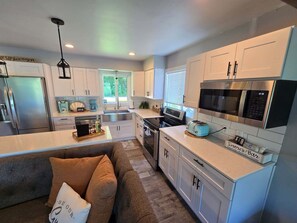 A modern kitchen with white cabinetry, stainless steel appliances, a built-in oven, and a coffee station.
