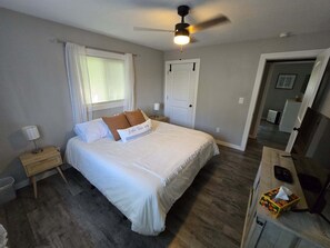 A bedroom with a bed, a nightstand, a ceiling fan, a window with curtains, and a door.