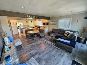 A modern living room with a fireplace, a sofa, a coffee table, and a dining area with a kitchen in the background.