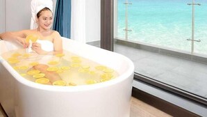 A bathtub filled with water and lemon slices, a person in a towel, and a view of the ocean through large windows. - Canvas Hotel (Da Nang)