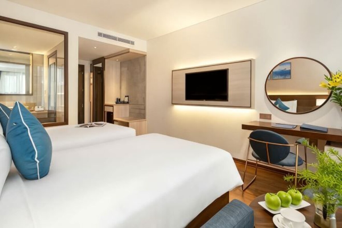 Ein Hotelzimmer mit einem großen Bett, einem Schreibtisch mit Stuhl, einem Flachbildfernseher, einem Spiegel und einer kleinen Pflanze.