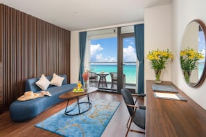 Een moderne hotelkamer met een blauwe bank, een eettafel, een stoel, een klein bijzettafeltje en uitzicht op de oceaan.