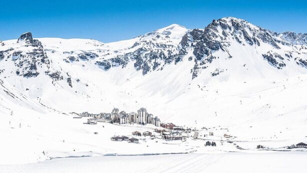 Paisaje nevado de montañas con un pueblo en primer plano.