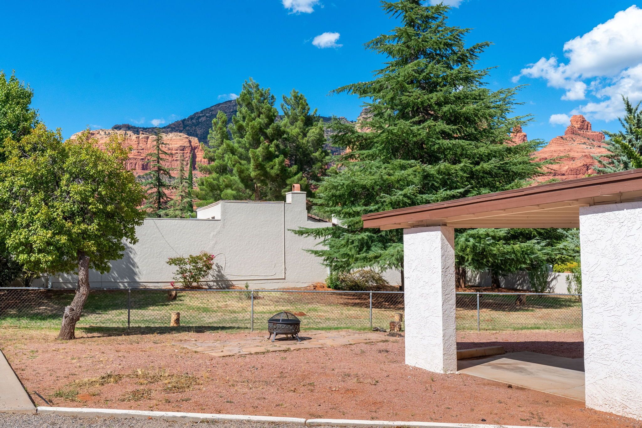 A fenced backyard with a barbecue grill, a covered patio, and a view of red rock formations.