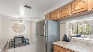 A kitchen with wooden cabinets, a stainless steel refrigerator, a dining table with chairs, and a window with a view of greenery. - Desert Dream Escape – Spacious 2BR Getaway (Sedona)