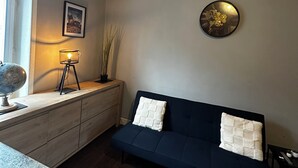 Une pièce chaleureuse avec un canapé bleu foncé, un globe terrestre posé sur une table d’appoint en bois, une lampe et un tableau encadré accroché au mur.