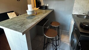 Une cuisine compacte dotée d’un plan de travail en granit, de deux tabourets, d’un lave-linge et d’un petit évier.