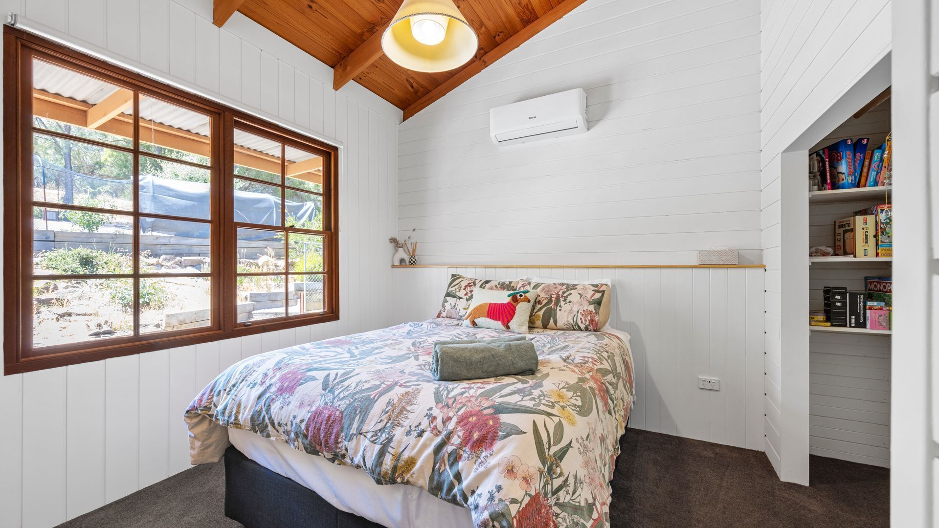 Une chambre à coucher avec un lit, une fenêtre, un appareil de climatisation et une bibliothèque.