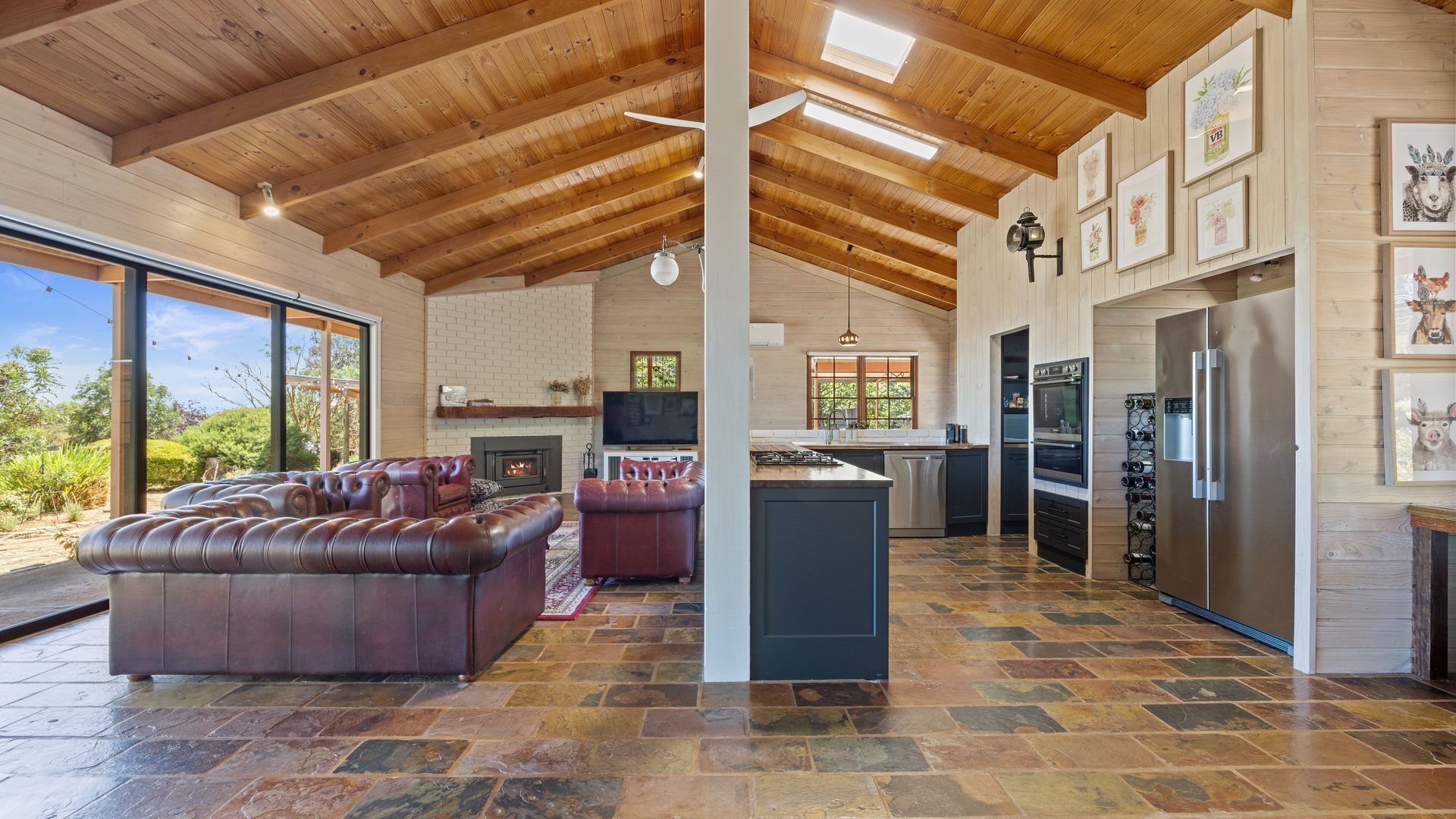 A spacious living area with a fireplace, leather sofa, and a kitchen with a large refrigerator and wine rack.