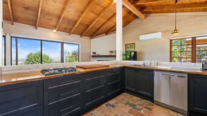 A modern kitchen with a large island, black cabinets, a stainless steel dishwasher, and a view through large windows. - Country Escape - 3BR Home with Panoramic Views (Mansfield)