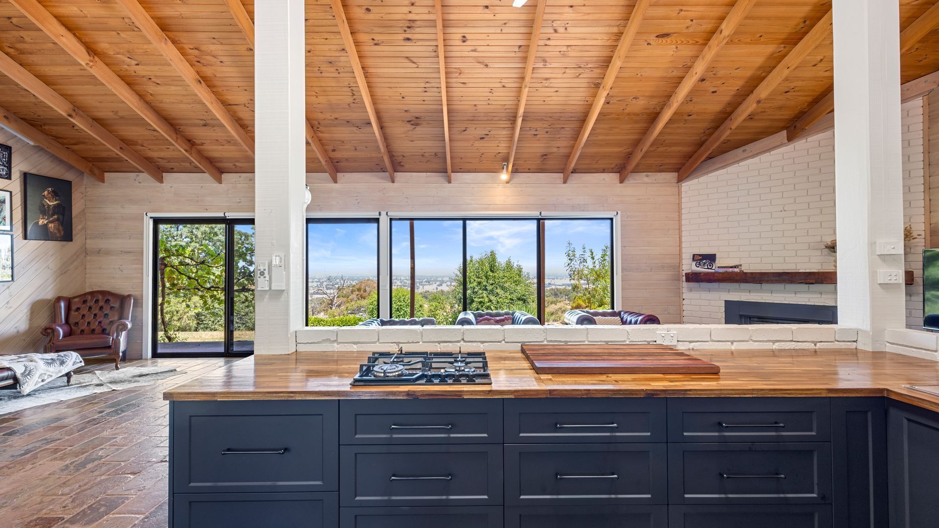 A modern kitchen with a large island, black cabinets, and a view of the outdoors through large windows.