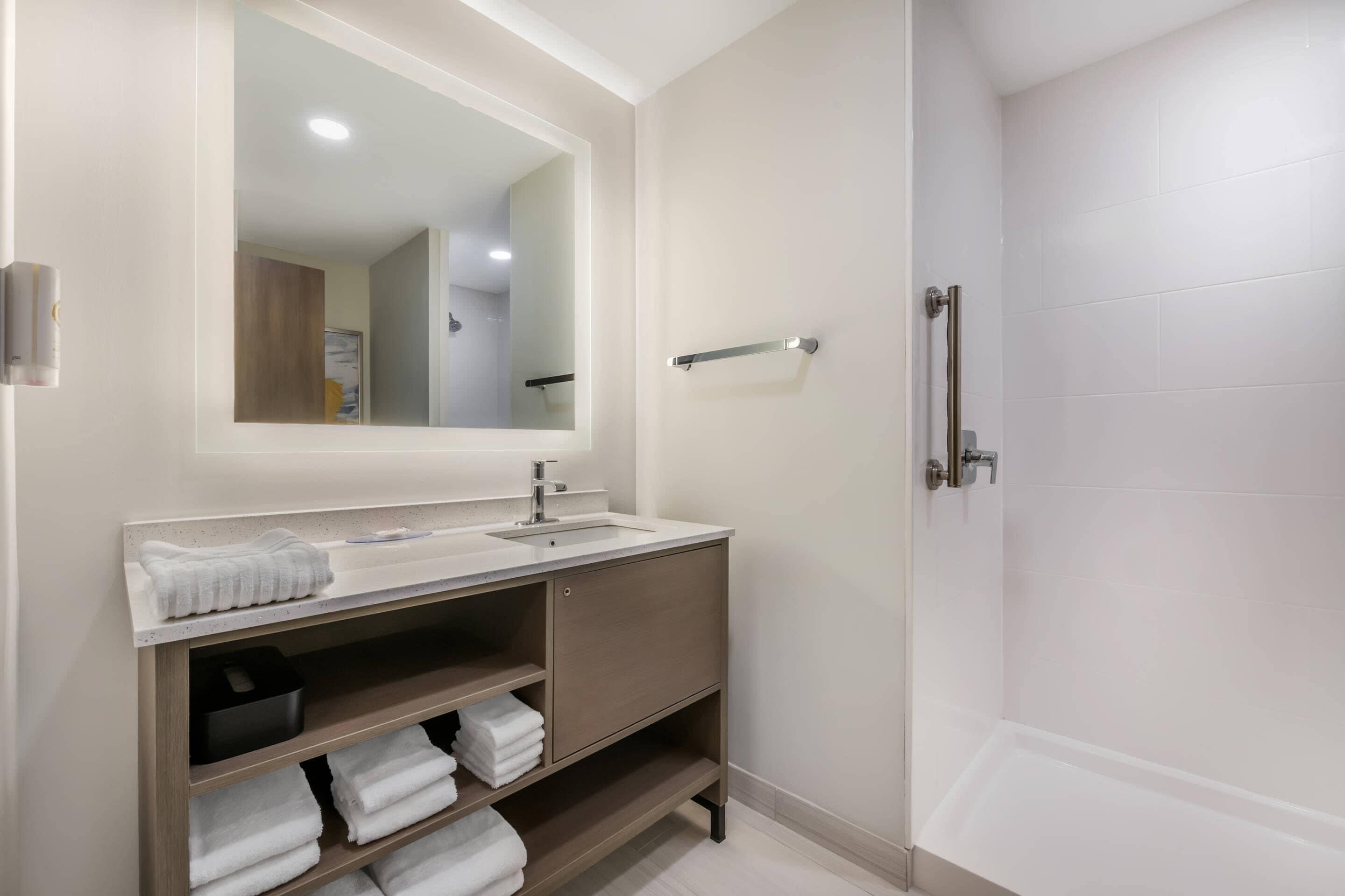 A modern bathroom with a large mirror, a sink, and a shower.