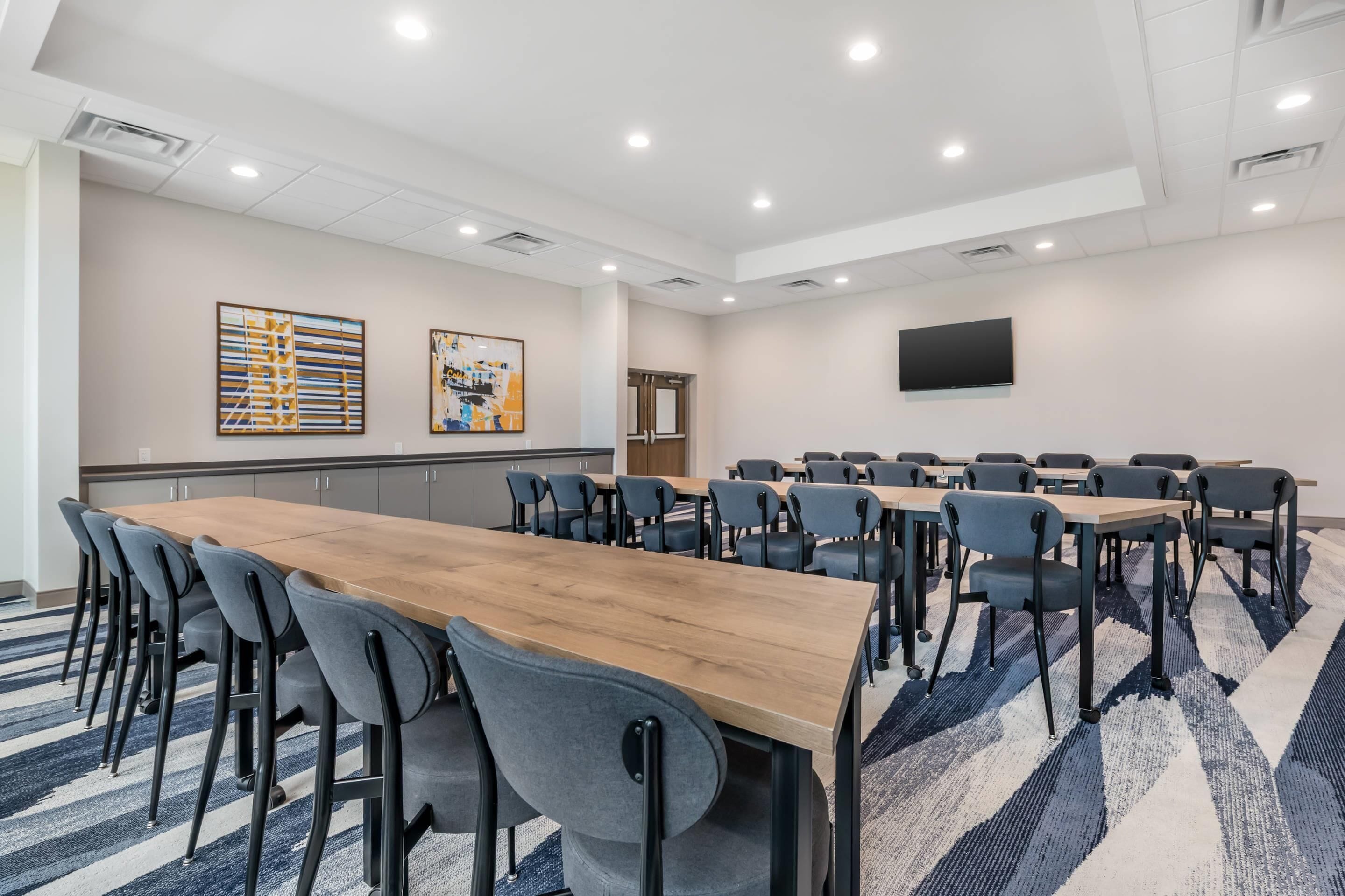 Un salón de conferencias con una larga mesa de madera, múltiples sillas, un televisor de pantalla plana en la pared y obras de arte en las paredes.