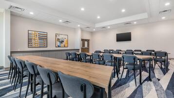 Un salón de conferencias con una larga mesa de madera, múltiples sillas, un televisor de pantalla plana en la pared y obras de arte en las paredes.