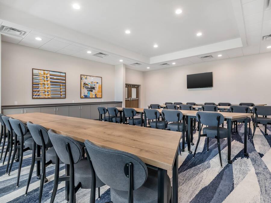 Un salón de conferencias con una larga mesa de madera, múltiples sillas, un televisor de pantalla plana en la pared y obras de arte en las paredes.
