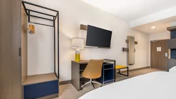 A hotel room with a bed, a desk with a chair, a TV mounted on the wall, and a wardrobe.