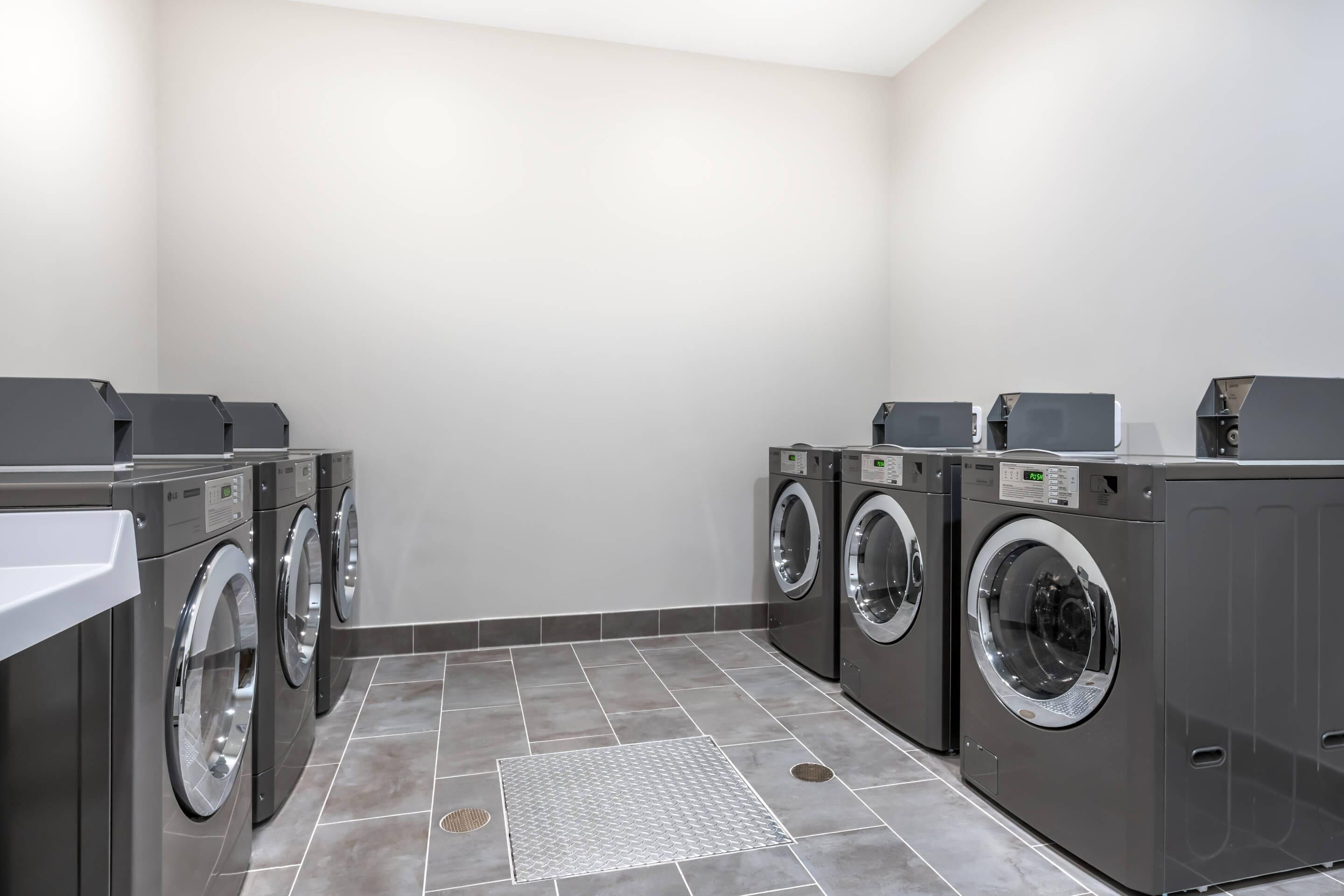 A laundry room with four front-loading washing machines and a sink.