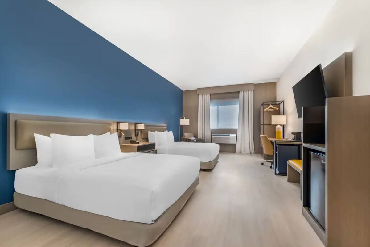 Ett hotellrum med en stor säng, ett skrivbord, en stol, en TV och ett fönster med gardiner.
