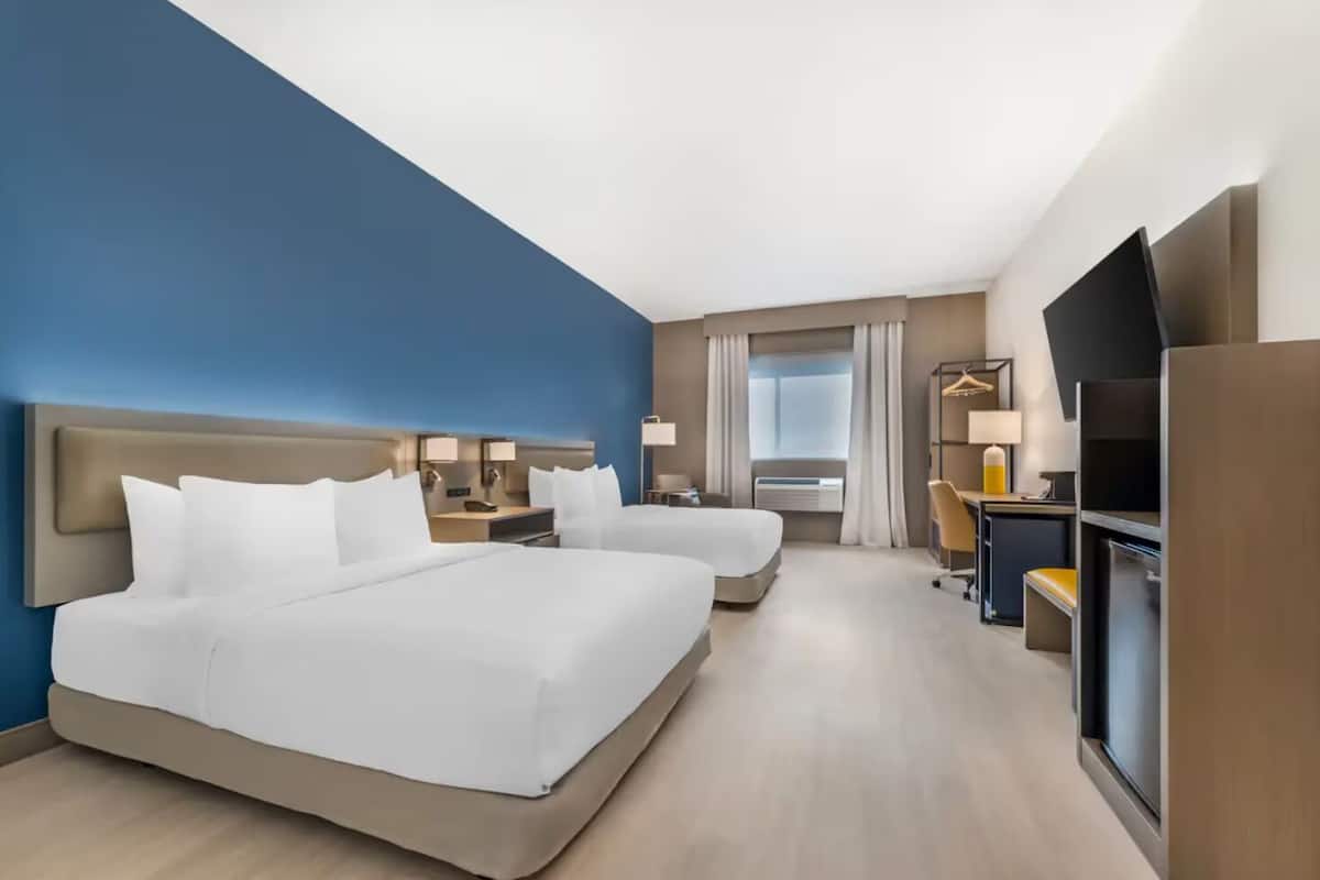Una habitación de hotel con una cama grande, un escritorio, una silla, un televisor y una ventana con cortinas.