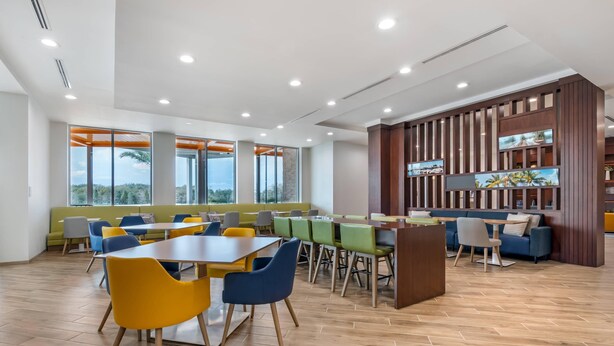 Un comedor moderno con varias mesas y sillas, ventanas amplias y una pared de madera decorada con obras de arte.