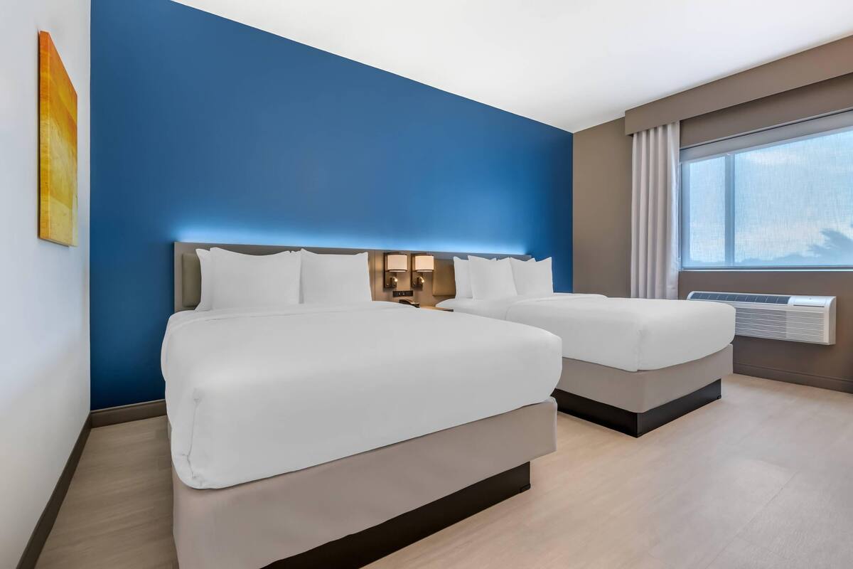 Ett hotellrum med två sängar, ett stort fönster och en väggmonterad luftkonditioneringsanläggning.