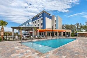 Un hotel con piscina, mobiliario exterior y zona cubierta.
