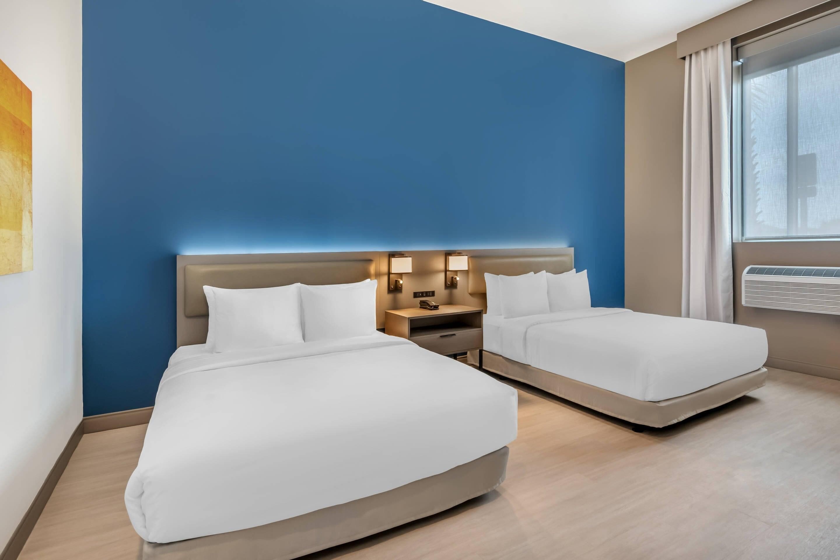 A hotel room with two beds, a nightstand with lamps, and a window with curtains.