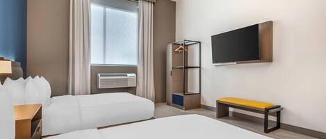 Una habitación de hotel con una cama grande, un banco, un armario, un televisor y una ventana con cortinas.