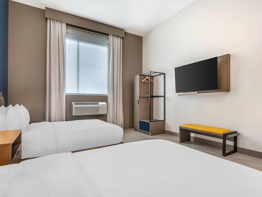 Une chambre d’hôtel avec un grand lit, une banquette, une armoire, une télévision et une fenêtre avec des rideaux.