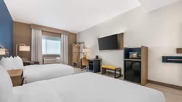 A hotel room with two beds, a desk, a chair, a TV, a mini-fridge, and a window with curtains.