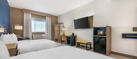 A hotel room with two beds, a desk, a chair, a TV, a mini-fridge, and a window with curtains.