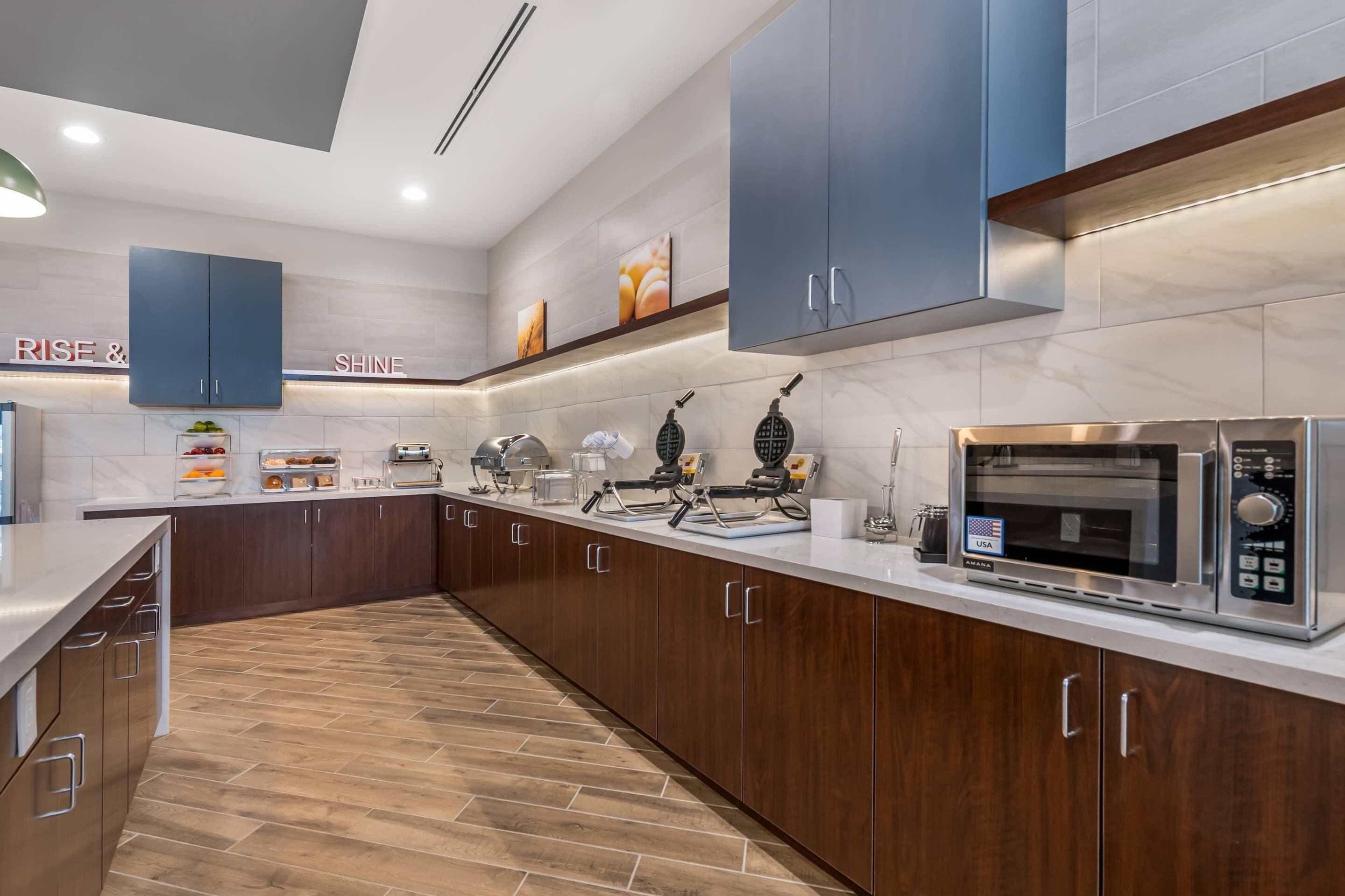 Una cocina moderna con armarios de madera, un microondas de acero inoxidable y una encimera con varios electrodomésticos.