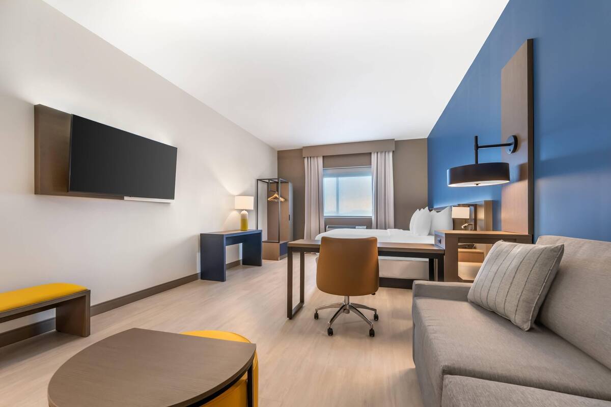 Ett modernt hotellrum med en säng, en soffa, ett skrivbord och en tv som är monterad på väggen.