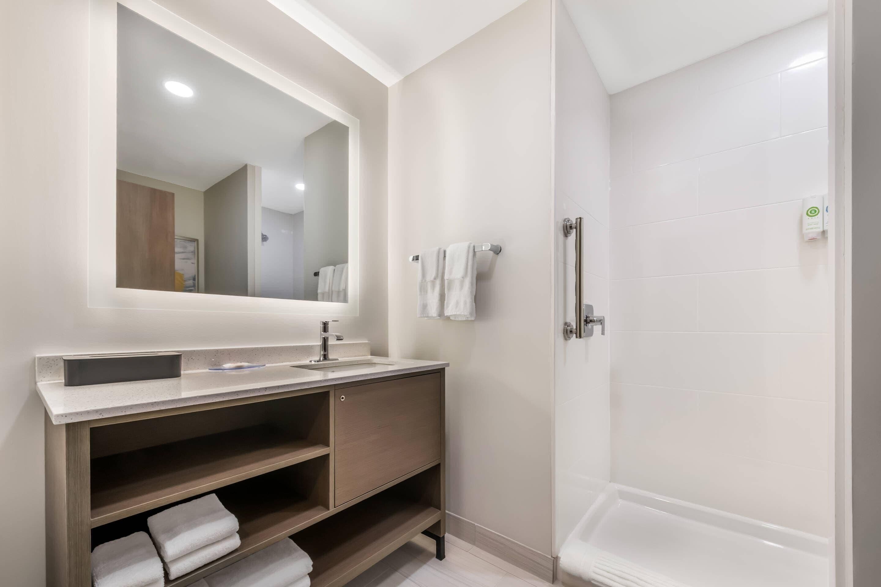 A modern bathroom with a large mirror, a sink, a vanity, and a walk-in shower.
